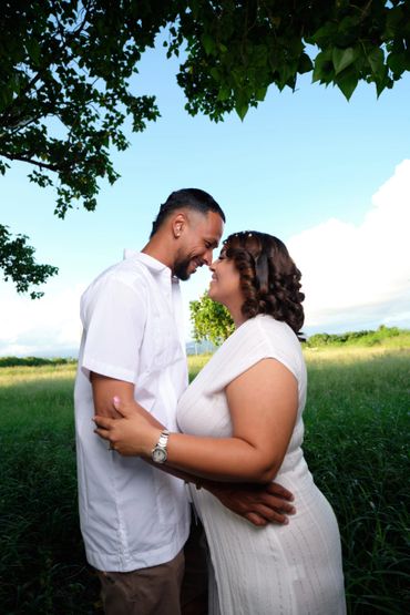 Couple embracing lovingly outdoors with a bright blue sky and greenery.
