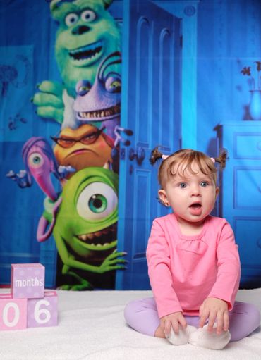 A surprised baby girl sitting with Monsters, Inc. characters in the background.