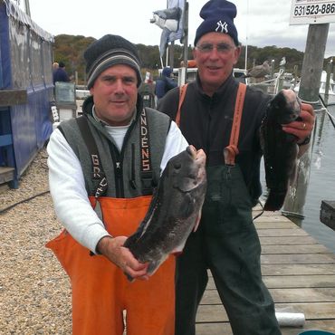 Two fishermen holding large fish at a dock.