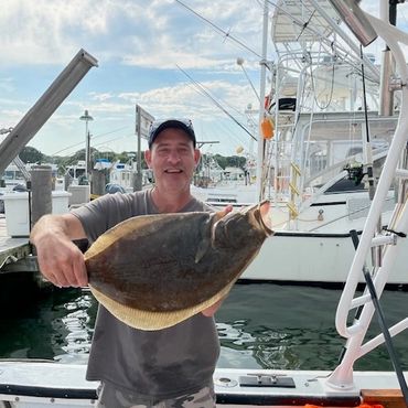 Man holding a large fish on a boat at a marina.