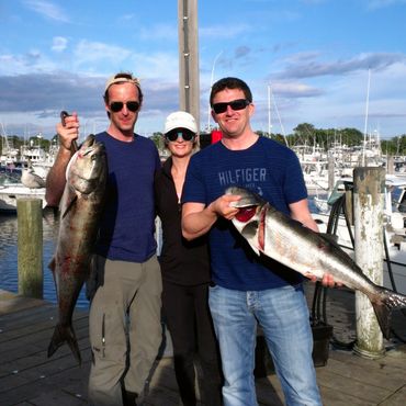 Three people holding big fish at a marina.