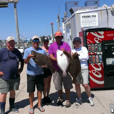 Group of five people holding fish by a dock.