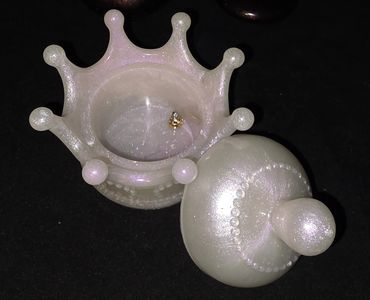 Pearlescent crown-shaped jewelry box with a shiny lid on black background.