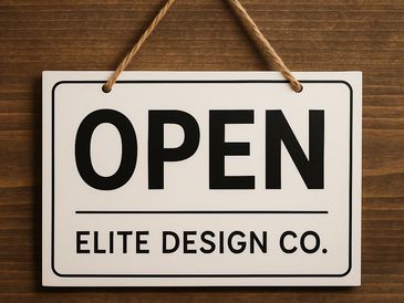 A white 'OPEN' sign with 'ELITE DESIGN CO.' text hanging on a wooden wall.