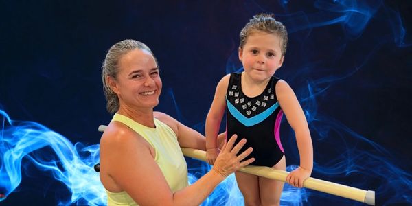 Woman helping a young girl on a ballet barre.
