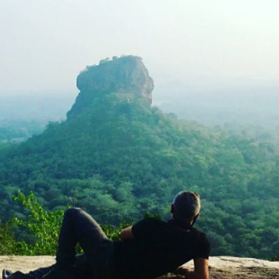 Person relaxing and admiring a large rock formation surrounded by forest.