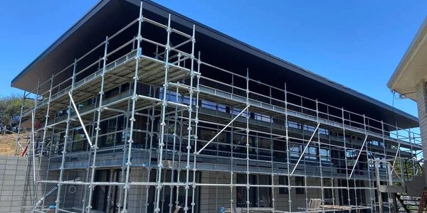 Modern building under construction with metal scaffolding and a clear blue sky.