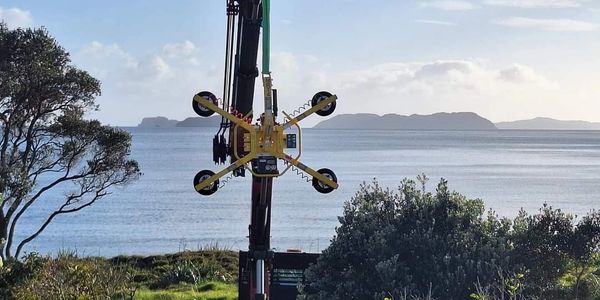 Crane lifting a yellow suction device near the sea with islands in the background.