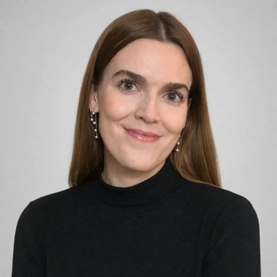 Smiling woman with long brown hair in black top against a plain background.