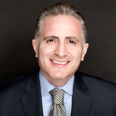 Smiling middle-aged man in a suit and patterned tie against a dark background.