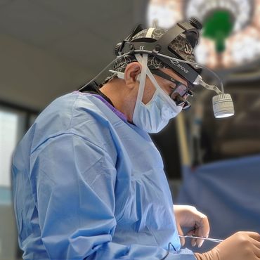 Surgeon focused during a procedure, wearing protective gear and a headlamp.