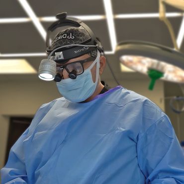 Surgeon in blue scrubs and headlamp performing surgery.