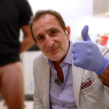 Man in a light suit giving a thumbs up wearing a blue glove.