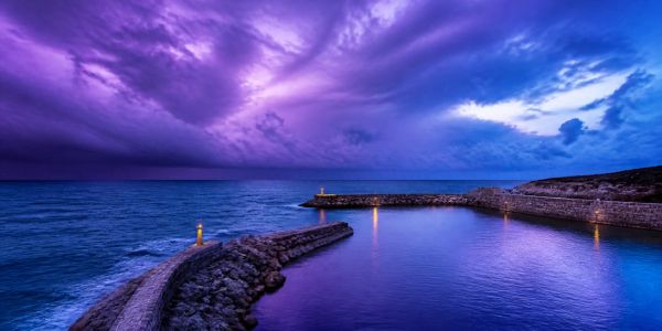 Dramatic purple twilight over a rocky harbor.