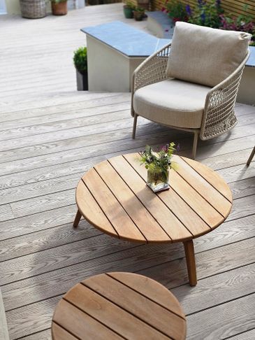 Cozy outdoor seating area with wooden tables and a cushioned chair on a deck.