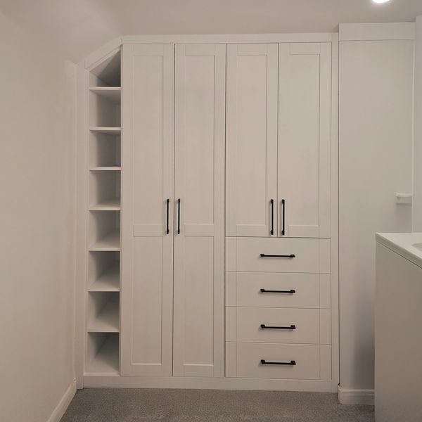 White built-in cabinets with black handles and open side shelves in a carpeted room.