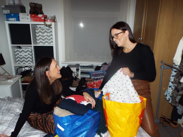 Two sisters sat on a bed organising a bag of clothes