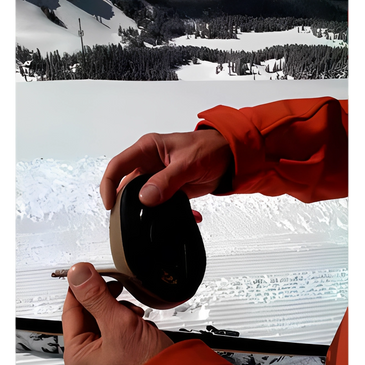 Hand adjusting or preparing a round black piece of gear in the snow.