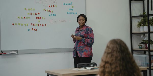 Teacher standing by whiteboard with colorful letters and numbers, teaching English to a student.