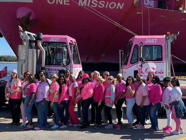 Group of women in pink shirts standing in front of two pink trucks.