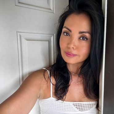 A woman with dark hair and a slight smile posing near a white door.