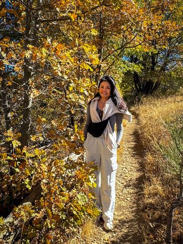 A woman hiking on a sunny autumn trail with colorful leaves.