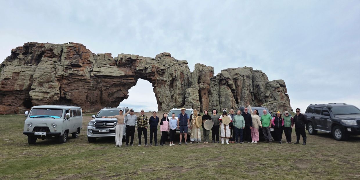 Group of people standing in front of a rock formation with vehicles.