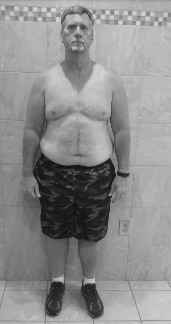 Man standing shirtless against tiled wall.