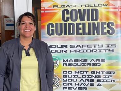 A public health nurse stands next to a poster listing COVID guidelines