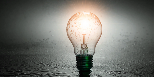 Glowing light bulb covered in water droplets on a wet surface.