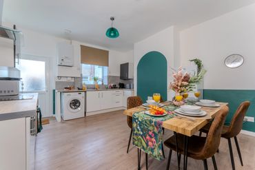 Modern kitchen-dining area with teal accents and a floral table runner.