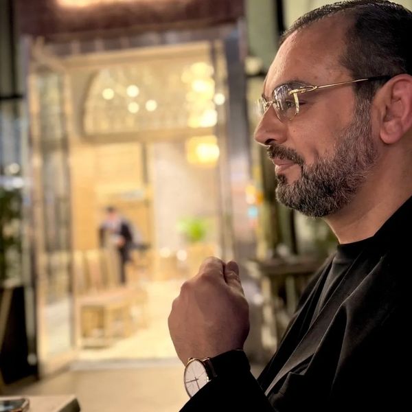 Man with glasses and watch sitting in a warmly lit cafe.