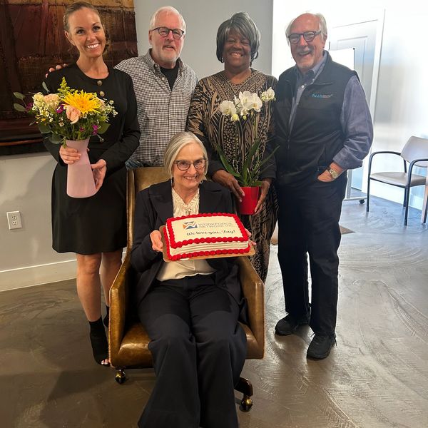 Group celebrating with flowers and cake, smiling warmly.