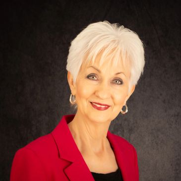 Elegant older woman with white hair wearing a red blazer, smiling warmly.