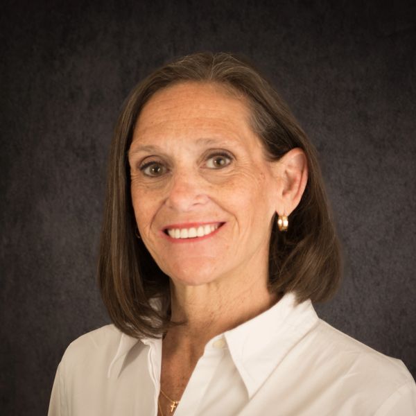 Professional portrait of a smiling woman with short brown hair and a white shirt.