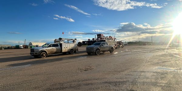 Two trucks on a wide dirt road under a partly cloudy sky with the sun low on the horizon.
