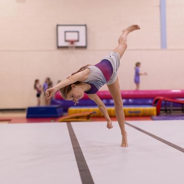 Young gymnast performing a one-handed cartwheel in a gymnasium.
