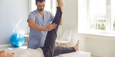 Physical therapist assists patient with leg stretch in a bright clinic.