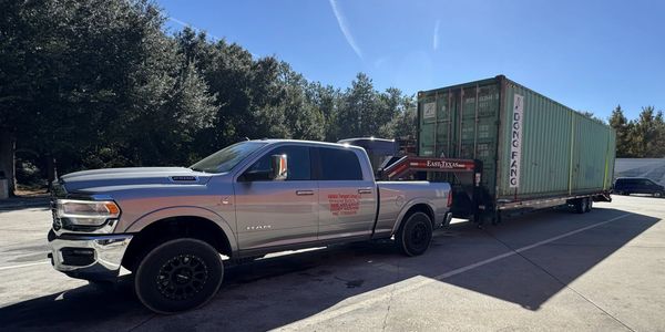 Silver RAM truck hauling a large green shipping container on a trailer.