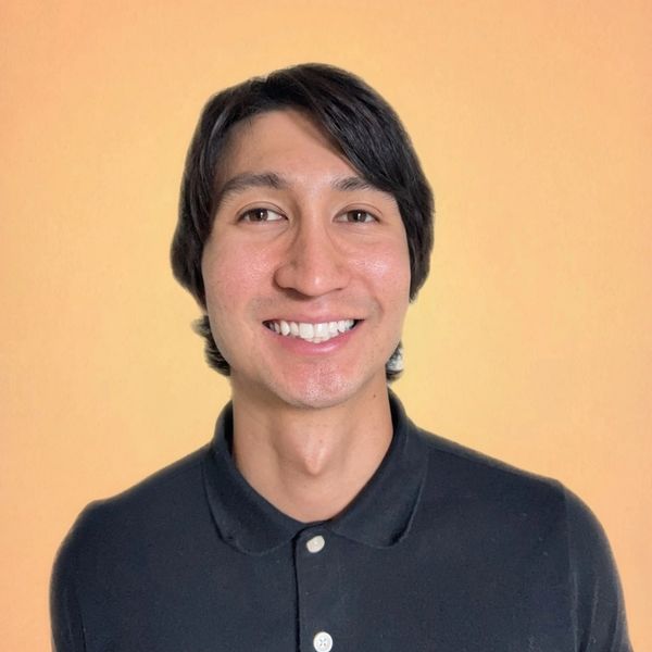 Young man smiling in a black polo shirt against a plain orange background.