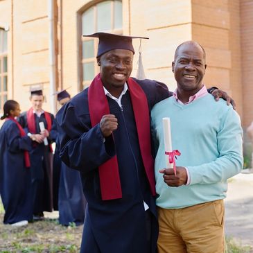 Graduate in cap and gown posing with a proud man holding a diploma.