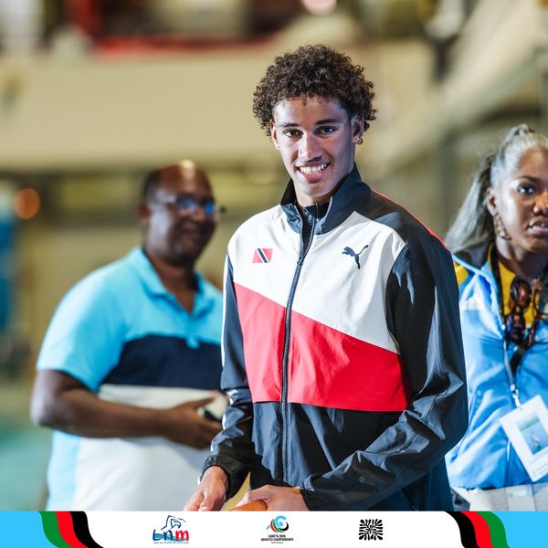 Young athlete smiling in a Puma jacket, with people in the background.
