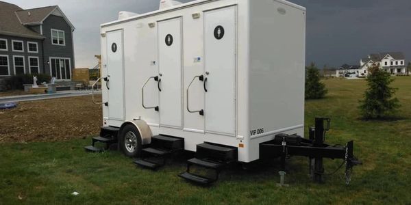 Portable restroom trailer with three units on a grassy area.