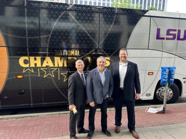 Three men posing in front of an LSU National Champions bus.