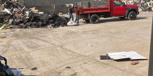Two people loading bags into a red truck at a scrap yard.
