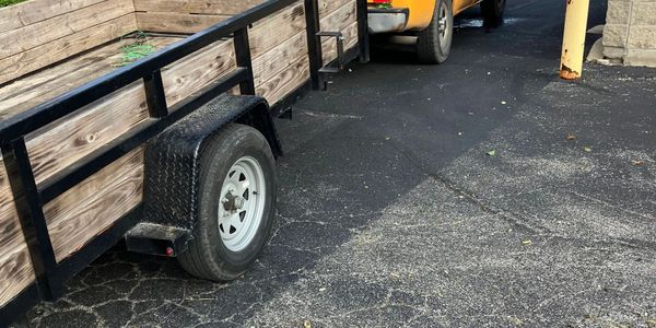Wooden utility trailer attached to a yellow vehicle on a cracked asphalt surface.