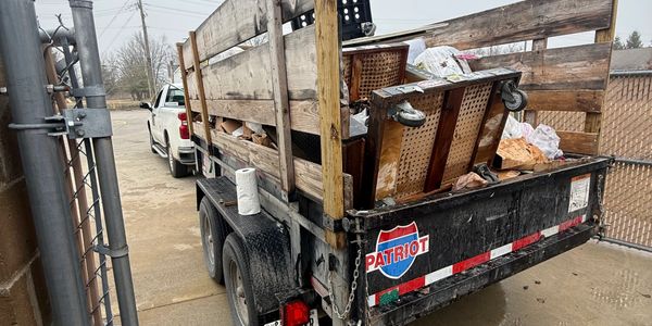 A pickup truck with a wooden trailer filled with old furniture and trash.