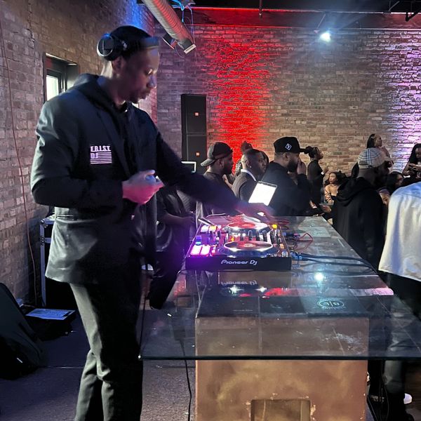 DJ performing at an indoor event with colorful lighting and a lively crowd.