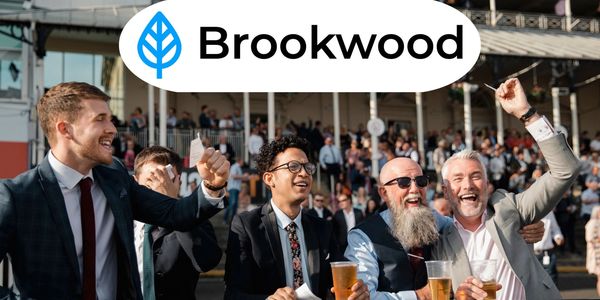 Excited men in suits cheering with drinks at a Brookwood event.