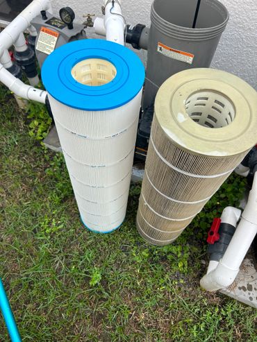 Two pool filter cartridges, one new and one used, standing upright beside pool equipment.